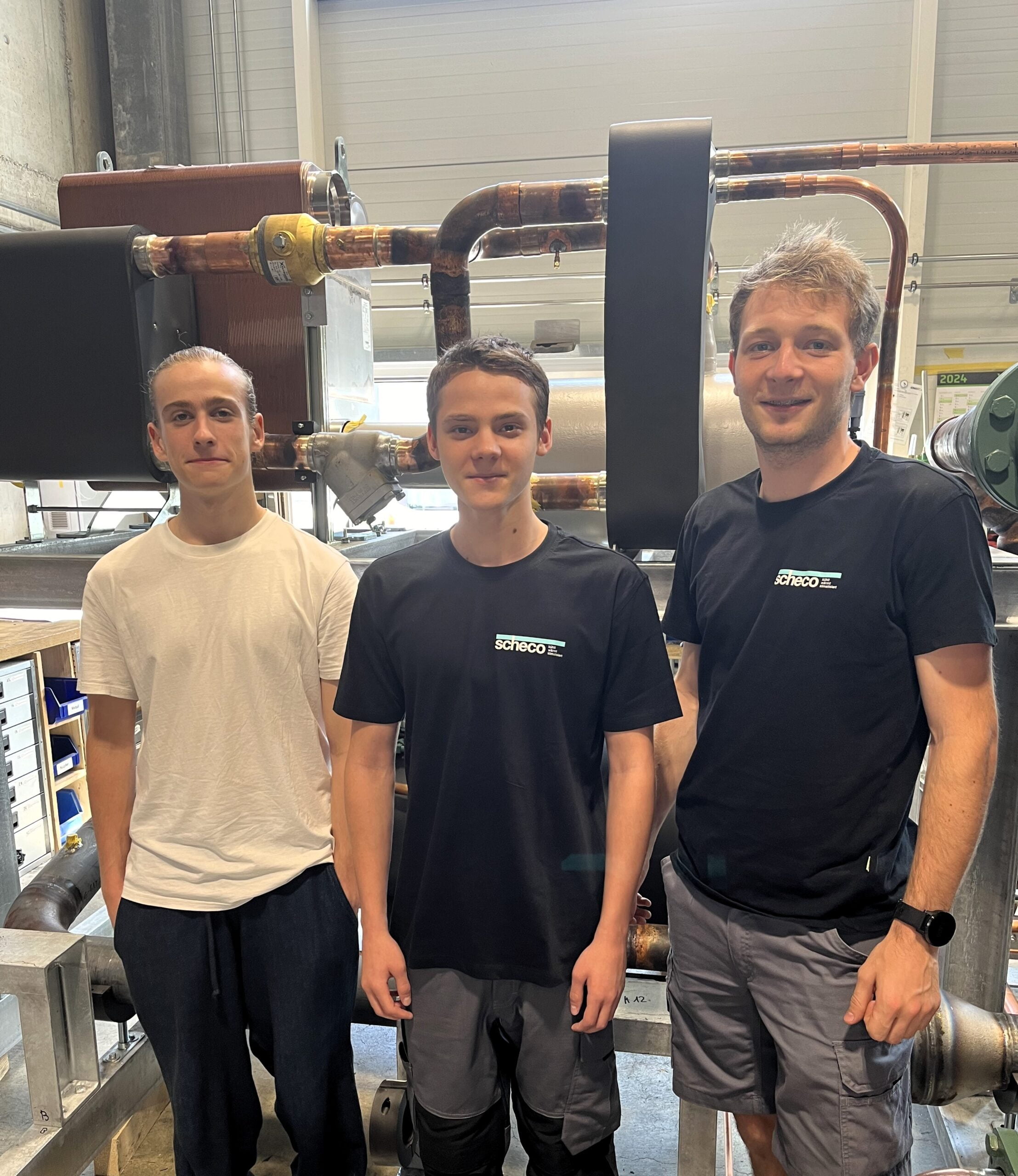 Die neuen Lehrlinge ab August 2024, Elias, Jaden, Sedric stehen in der Werkstatt vor einer Kälteanlage
