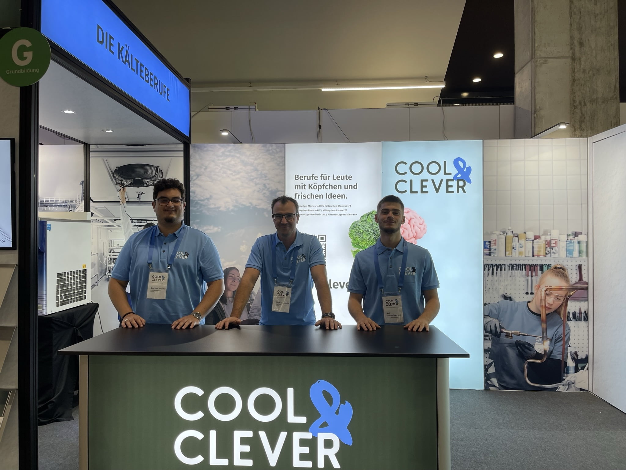 Georgios, Berufsbildner Roger und Noe am Stand der Ostschweizer Messe für Aus- und Weiterbildung. Alle drei stehen am Tisch von Cool & Clever und lachen in die Kamera.